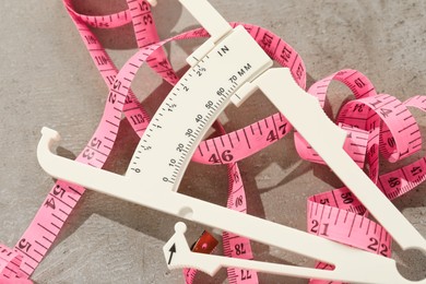 Plastic body fat caliper and measuring tape on grey table, closeup