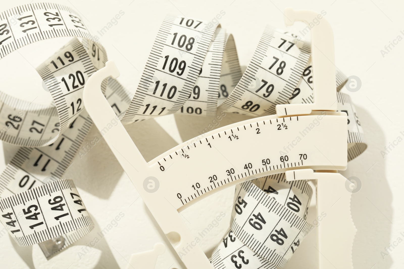 Photo of Plastic body fat caliper and measuring tape on white table, closeup