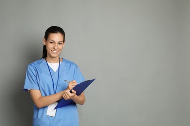 Photo of Portrait of smiling nurse with clipboard on grey background. Space for text