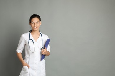 Portrait of smiling nurse with clipboard on grey background. Space for text