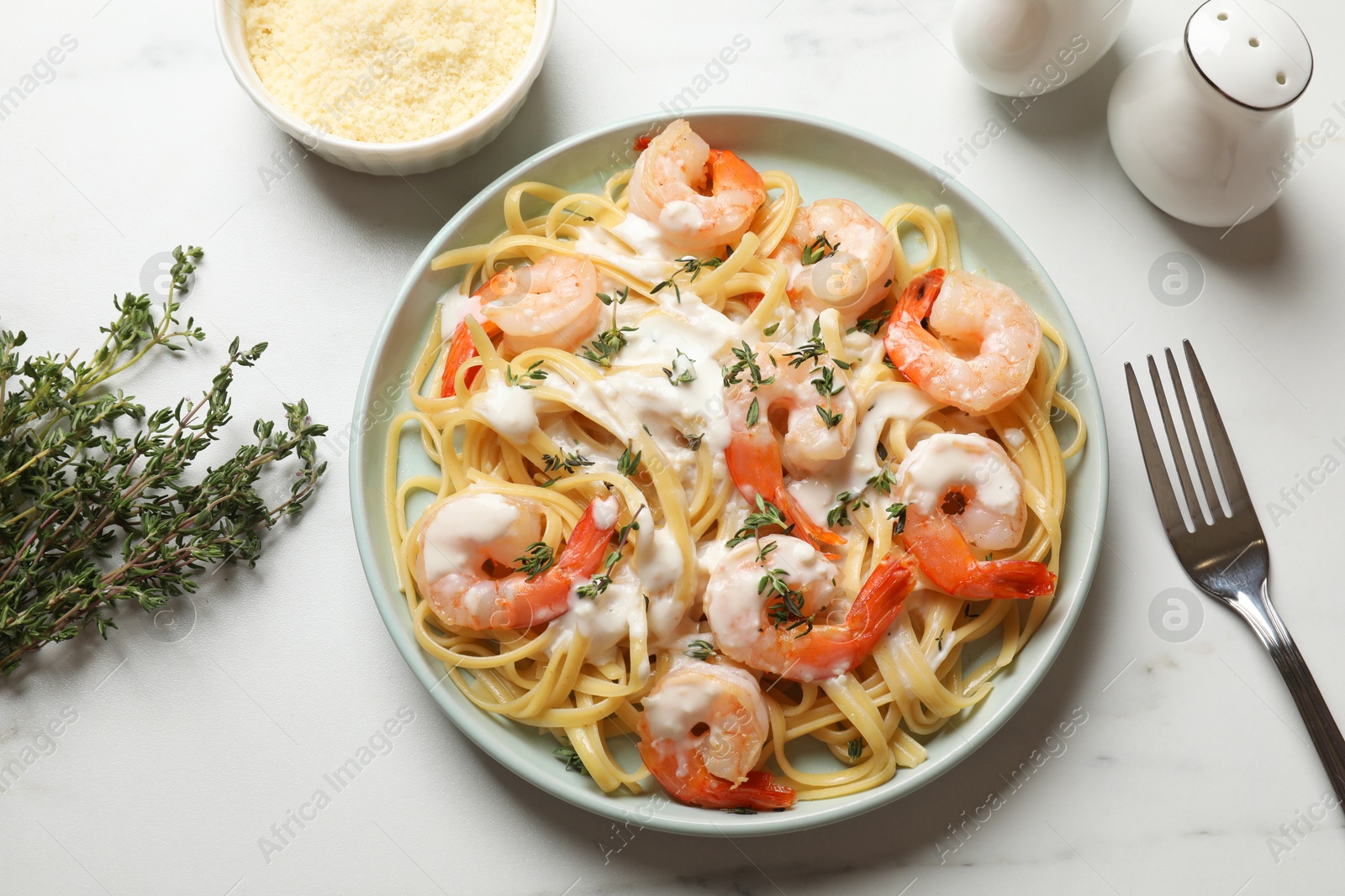 Photo of Delicious pasta with shrimps and creamy sauce served on white marble table, flat lay