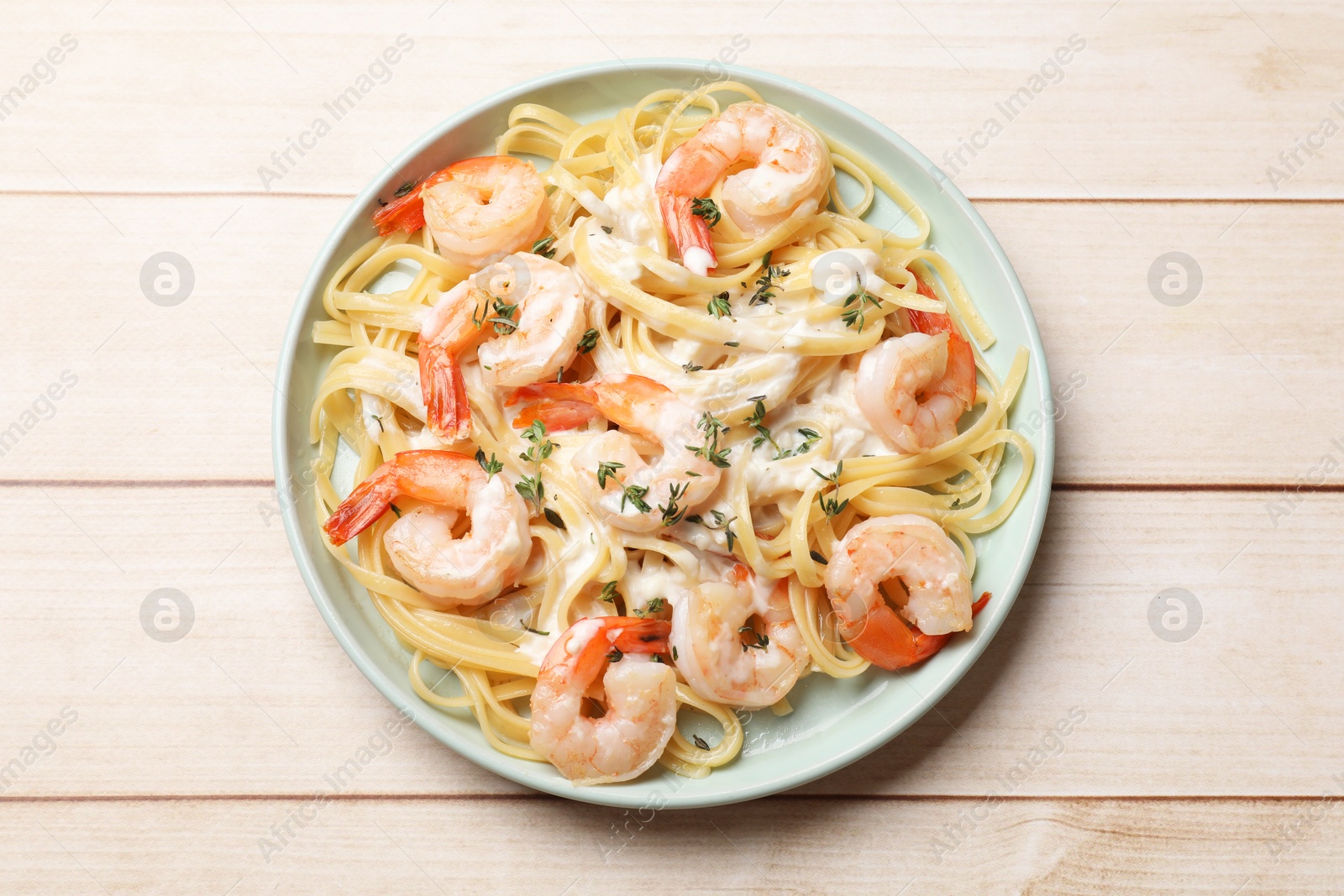 Photo of Delicious pasta with shrimps and creamy sauce on light wooden table, top view