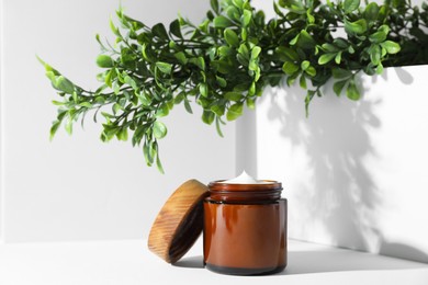 Photo of Facial cream in jar and floral decor on white table