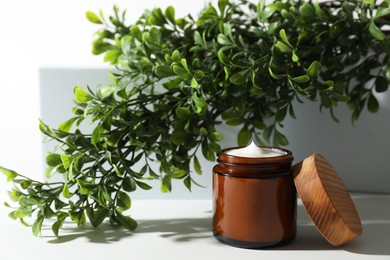 Facial cream in jar and floral decor on white table