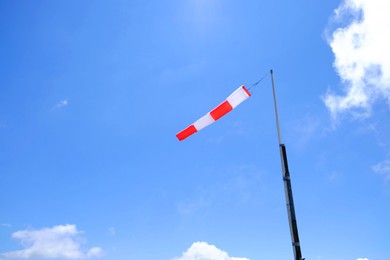 Striped windsock on pole against blue sky, space for text