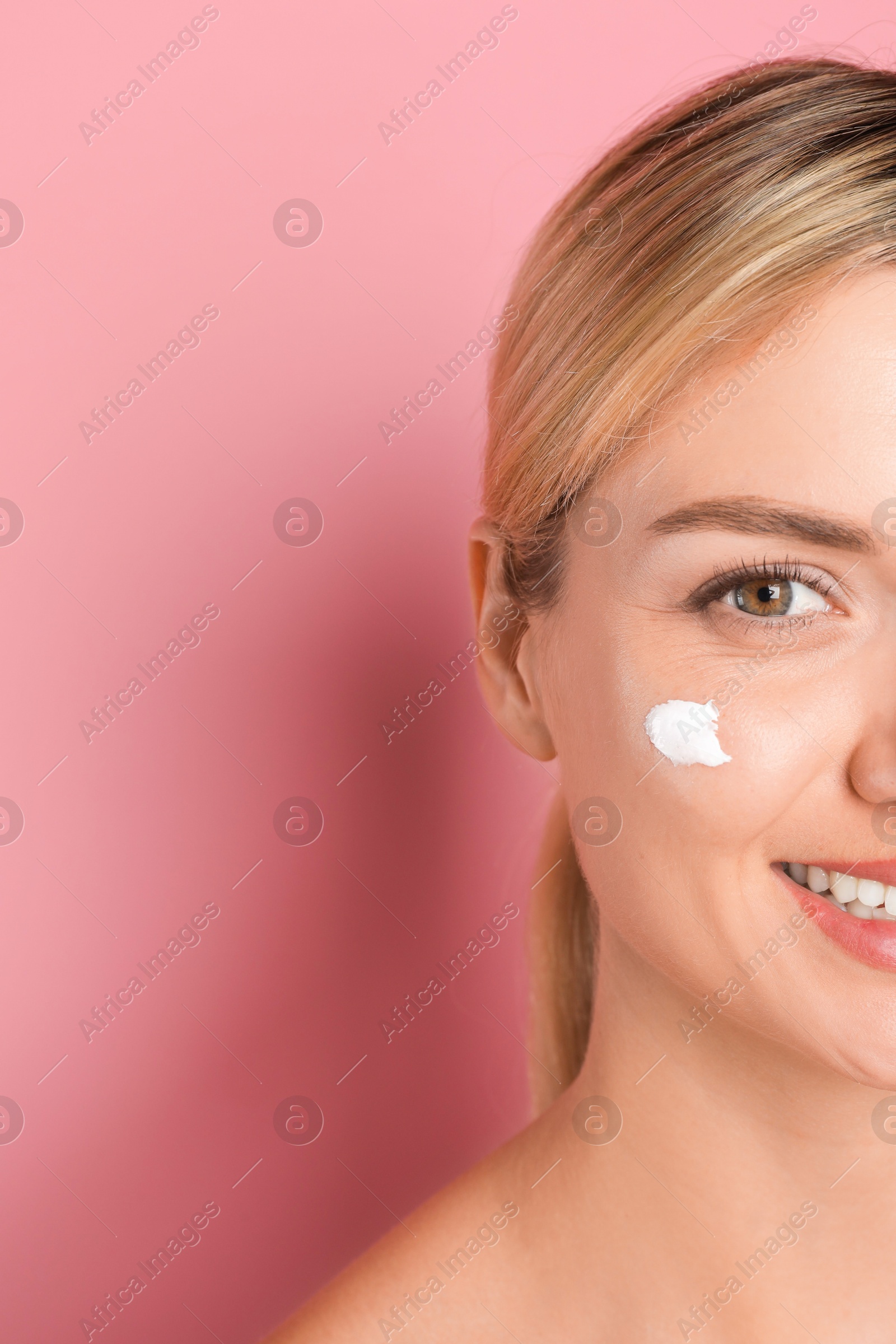 Photo of Beautiful woman with cream on her face against pink background, closeup