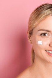 Beautiful woman with cream on her face against pink background, closeup