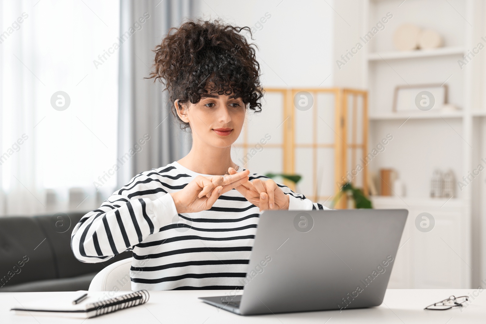 Photo of Young woman using sign language for communication during video call at white table indoors