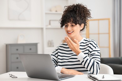 Young woman using sign language for communication during video call at white table indoors