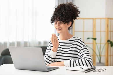 Photo of Young woman using sign language for communication during video call at white table indoors