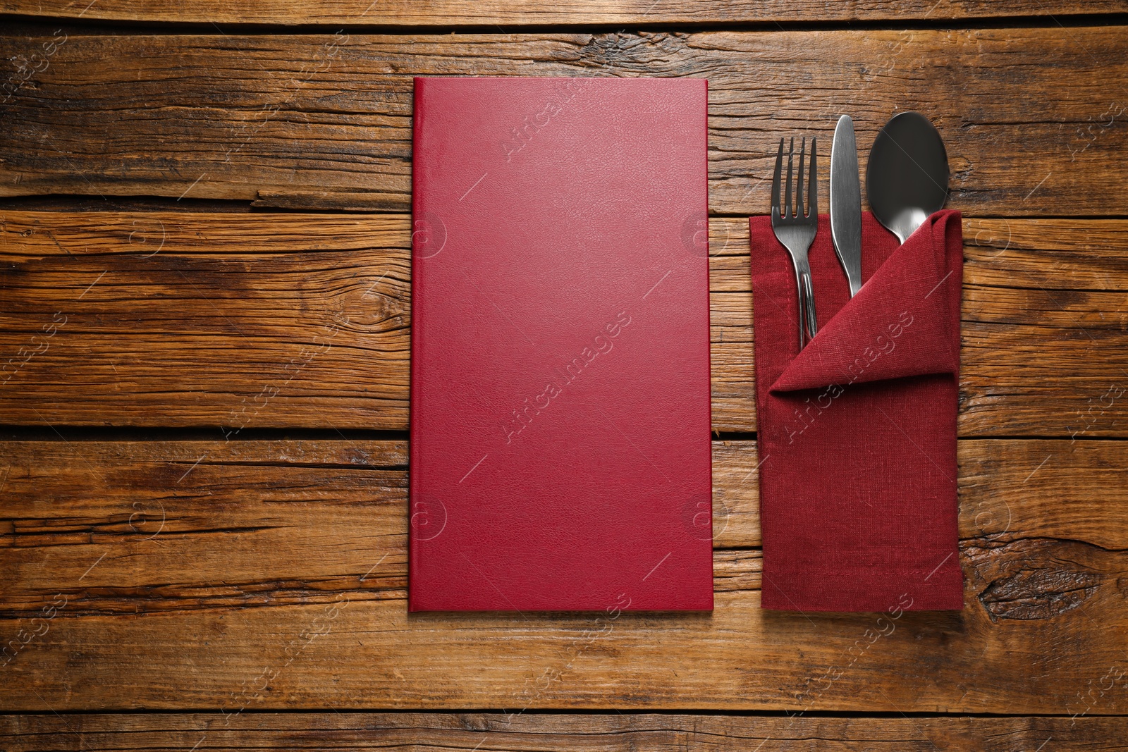 Photo of Hardcover menu and cutlery on wooden table, flat lay