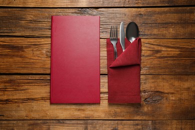 Photo of Hardcover menu and cutlery on wooden table, flat lay