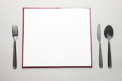 Photo of Hardcover notebook with empty sheets for menu design and cutlery on light grey table, flat lay