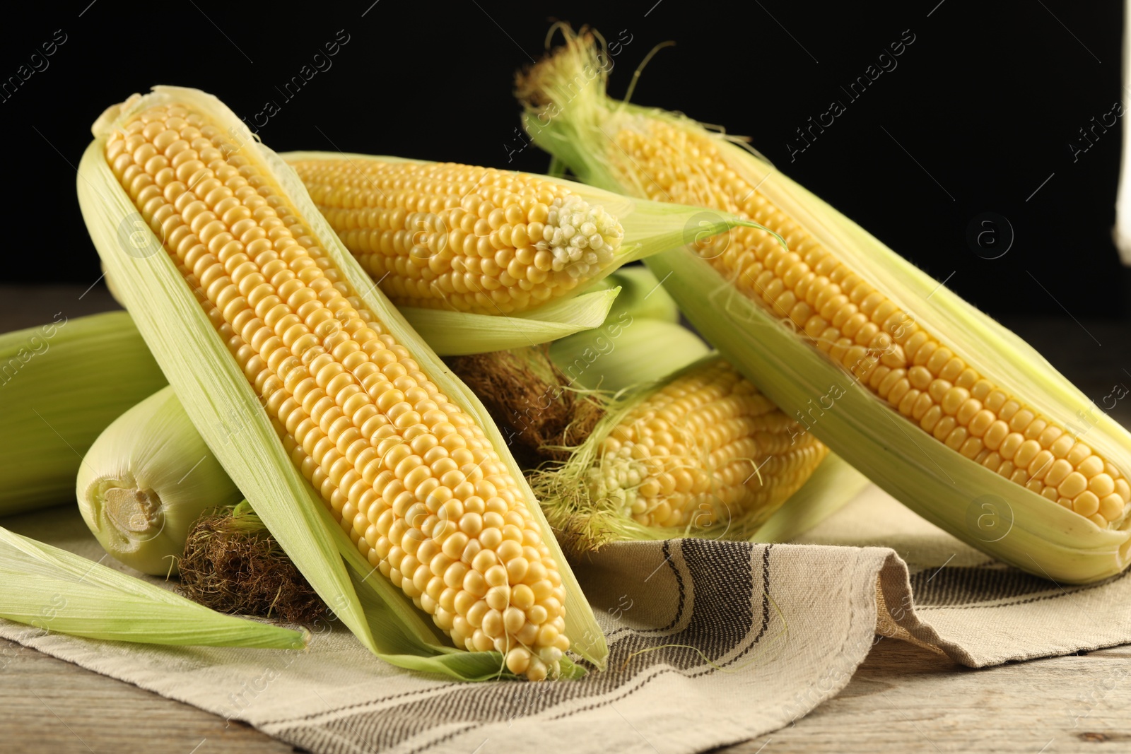 Photo of Many fresh ripe corncobs with green husks on wooden table