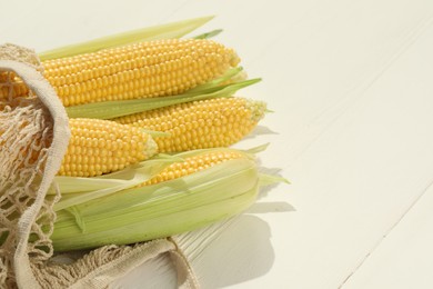 Many fresh ripe corncobs with green husks on white wooden table, closeup. Space for text