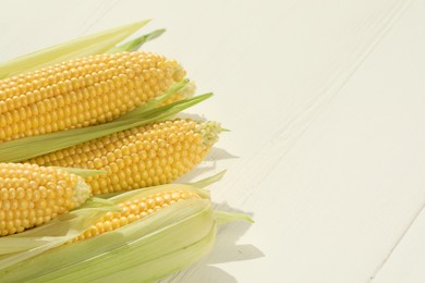 Photo of Many fresh ripe corncobs with green husks on white wooden table, closeup. Space for text