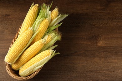 Photo of Many fresh ripe corncobs with green husks on wooden table, top view. Space for text