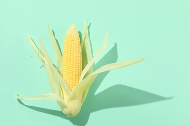 Photo of Fresh ripe corncob with green husks on turquoise background, top view. Space for text