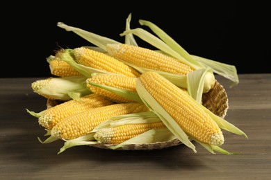 Photo of Many fresh ripe corncobs with green husks on wooden table