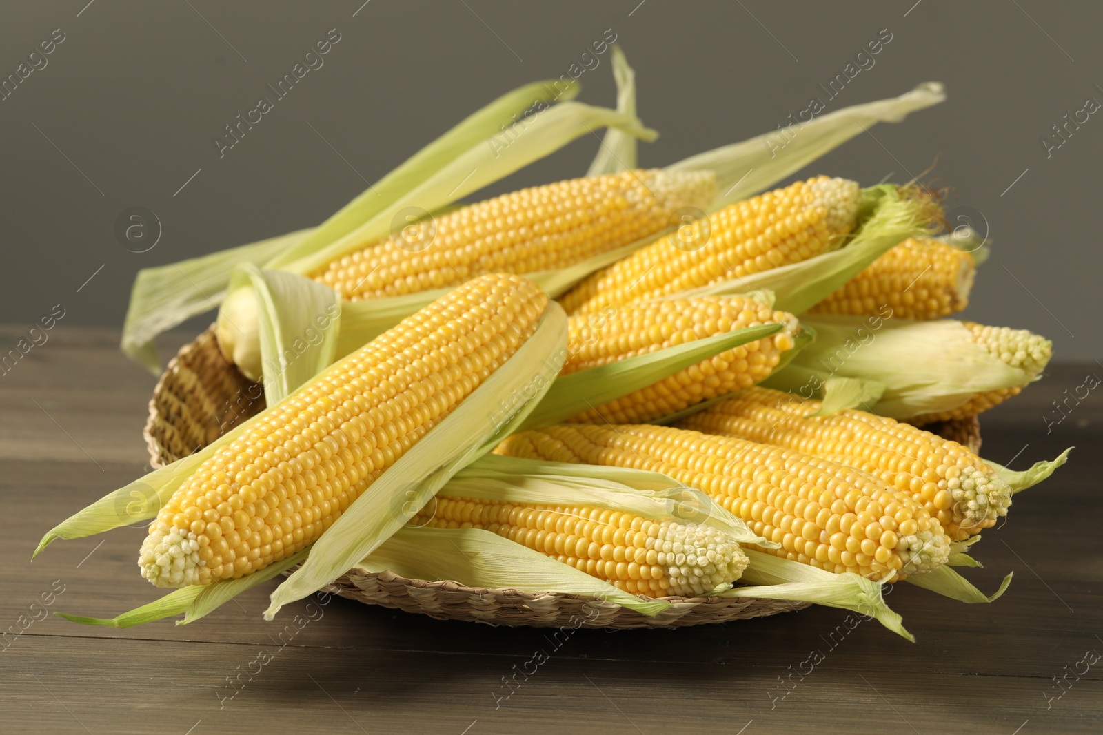 Photo of Many fresh ripe corncobs with green husks on wooden table