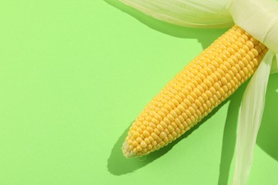 Fresh ripe corncob with husks on light green background, top view. Space for text