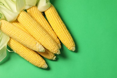 Photo of Many fresh ripe corncobs with husks on green background, top view. Space for text