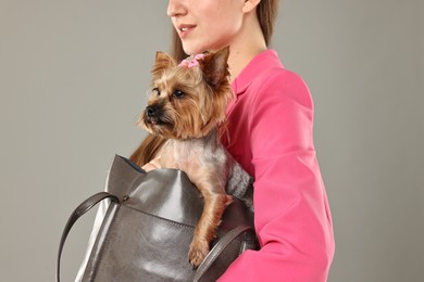 Photo of Woman carrying cute Yorkshire Terrier dog in bag on grey background, closeup