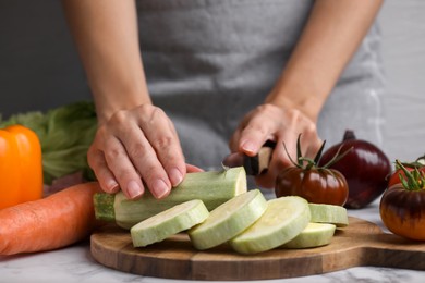 Photo of Cooking vegetable stew. Woman cutting zucchini at white marble table, closeup