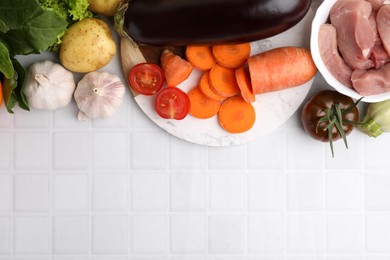 Photo of Different vegetables and raw meat for stew on white tiled table, top view. Space for text