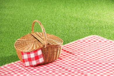 Photo of One picnic wicker basket with checkered napkin and blanket on green grass. Space for text