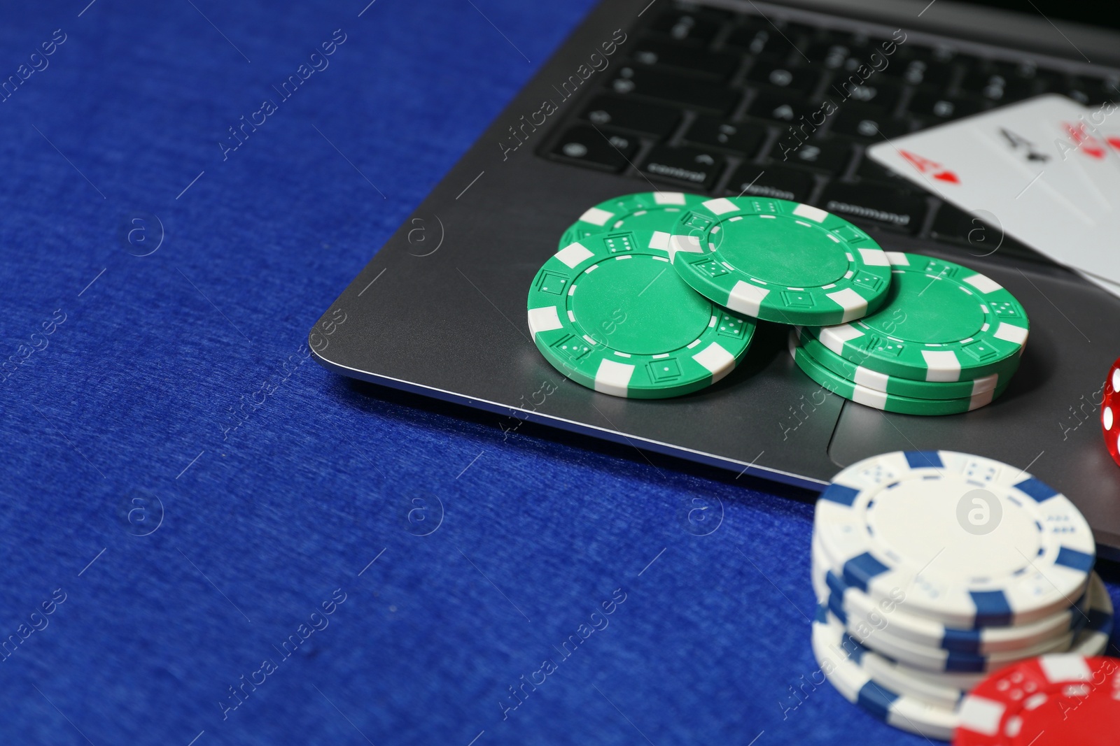 Photo of Poker chips, laptop and playing cards on blue table. Online game