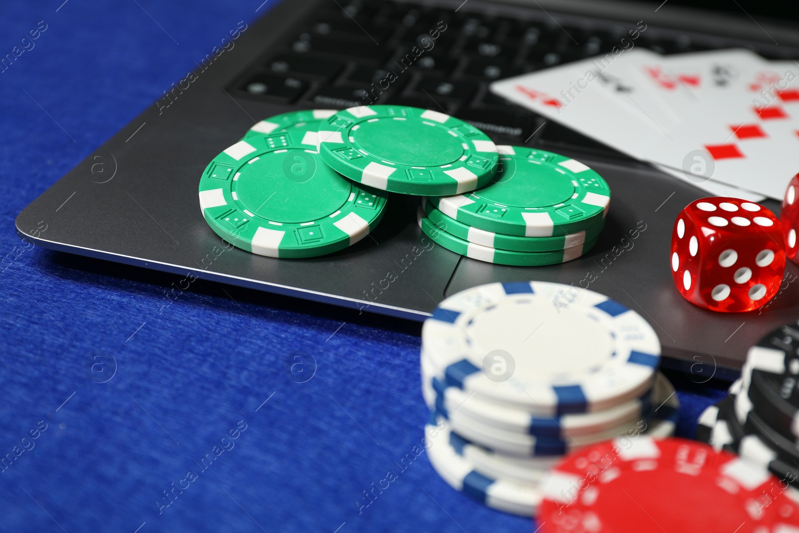 Photo of Poker chips, laptop, dice and playing cards on blue table. Online game