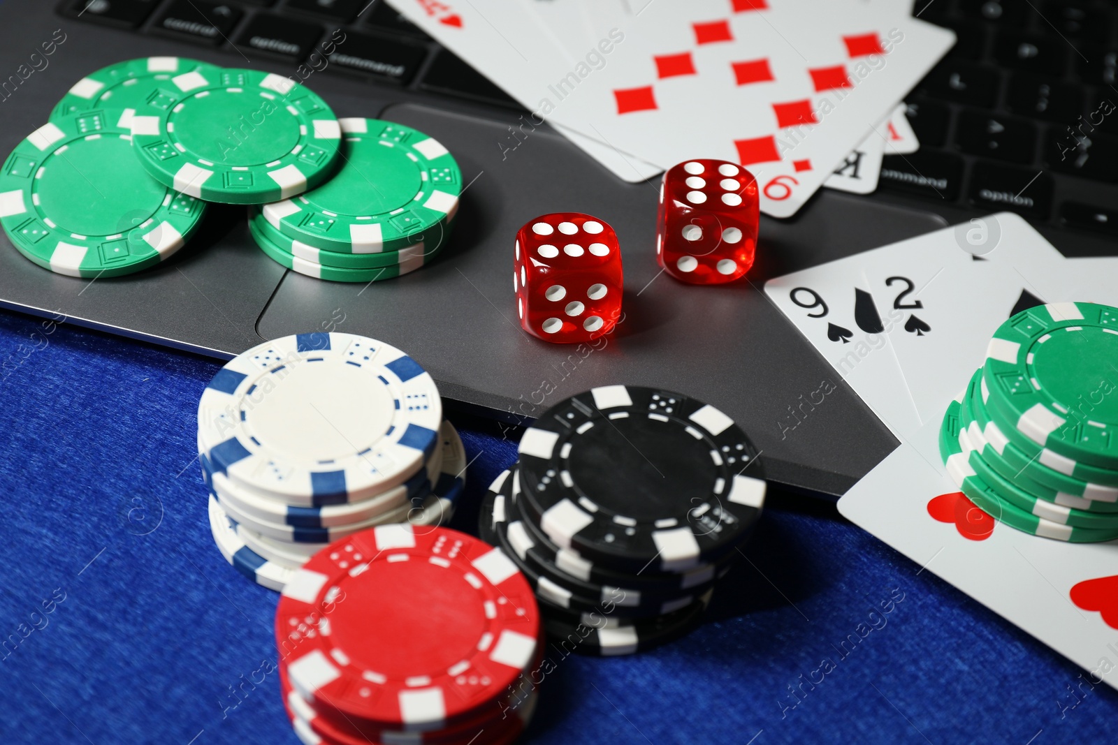 Photo of Poker chips, laptop, playing cards and dices on blue table. Online game