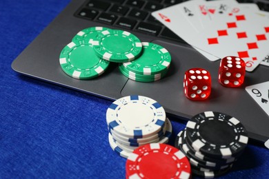 Photo of Poker chips, laptop, playing cards and dices on blue table. Online game