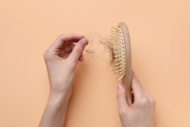 Woman taking her lost hair from brush on beige background, top view. Alopecia problem