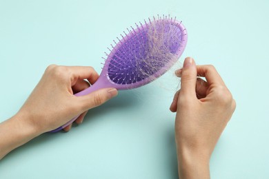 Woman taking her lost hair from brush on light blue background, closeup. Alopecia problem