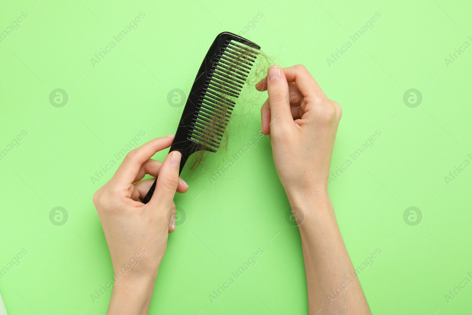 Photo of Woman taking her lost hair from comb on light green background, top view. Alopecia problem