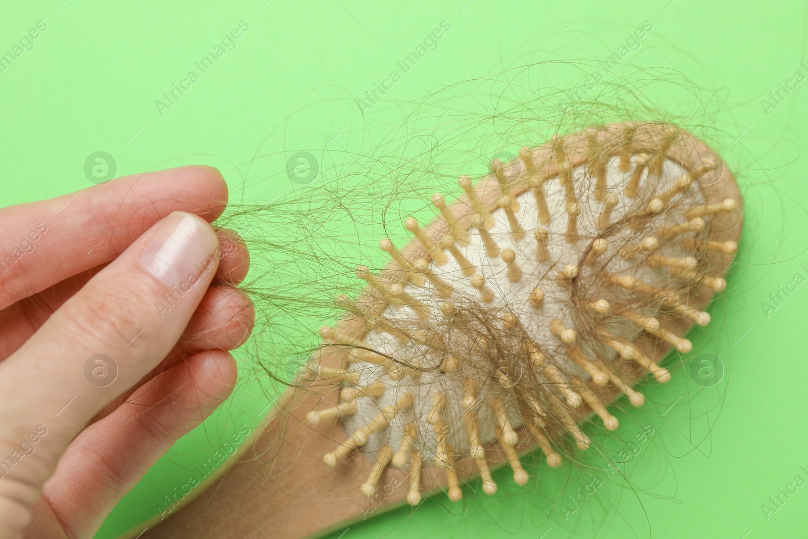 Photo of Woman taking her lost hair from brush on light green background, closeup. Alopecia problem