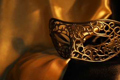 Photo of Beautiful golden carnival mask on silk fabric, closeup