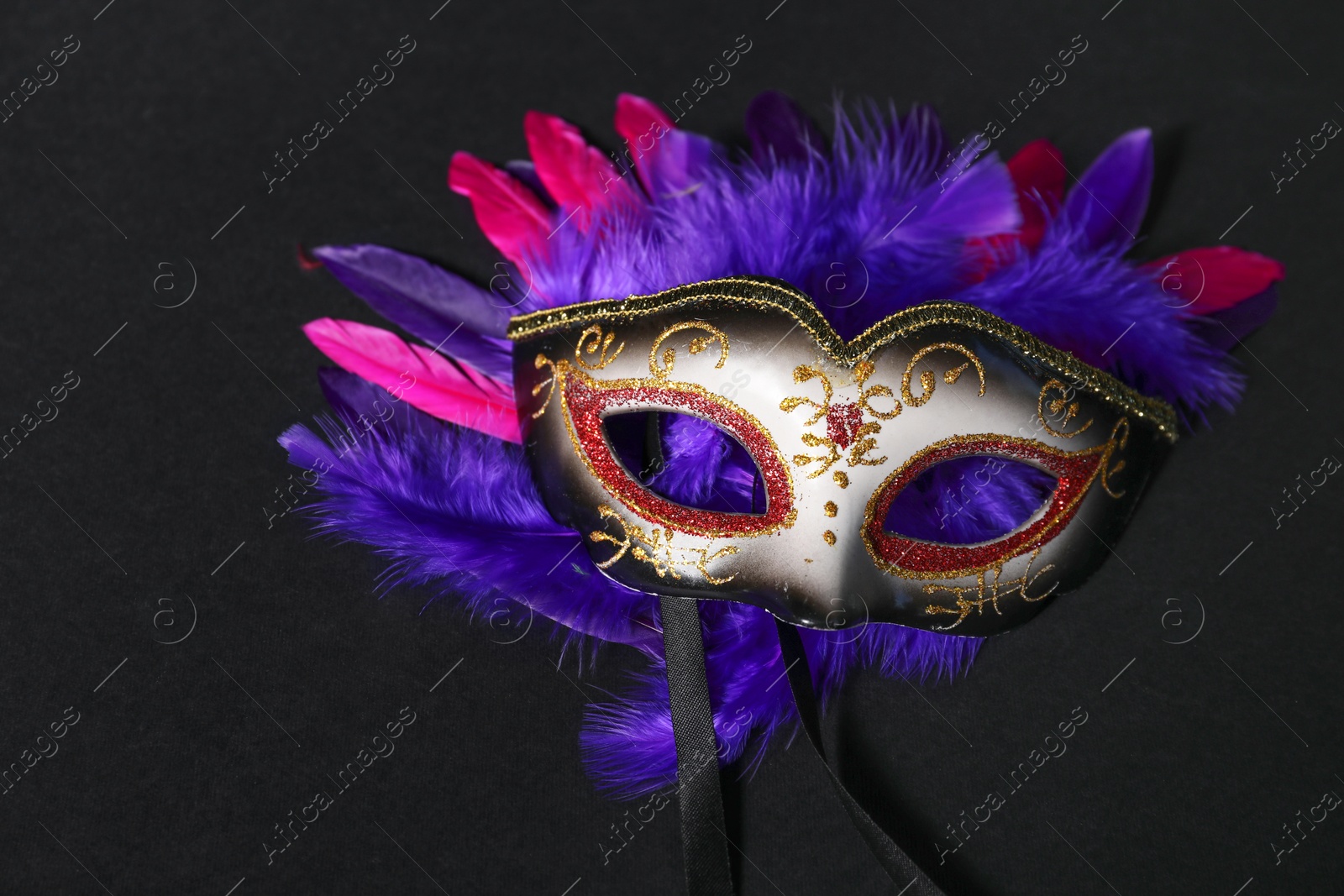 Photo of Beautiful carnival mask and bright feathers on black background, closeup