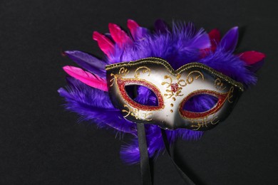 Beautiful carnival mask and bright feathers on black background, closeup