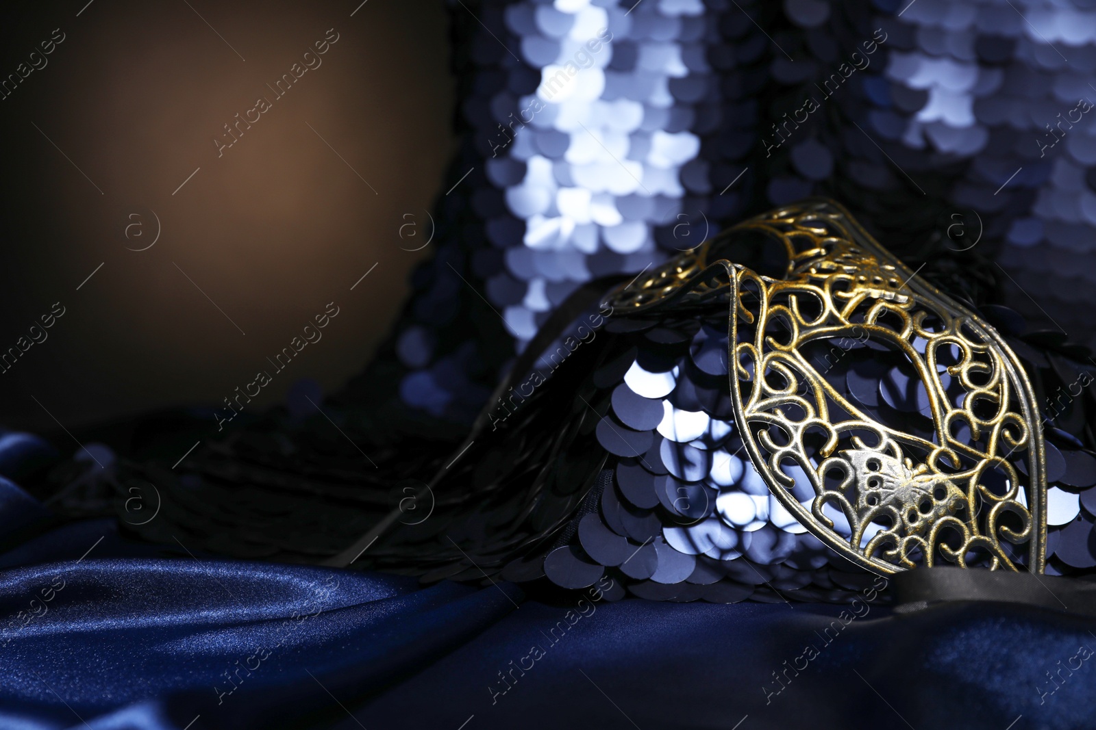 Photo of Beautiful carnival mask and fabric with golden sequins in darkness, closeup. Space for text