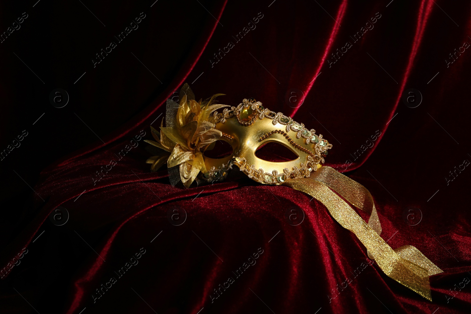 Photo of Beautiful golden carnival mask on red silk fabric