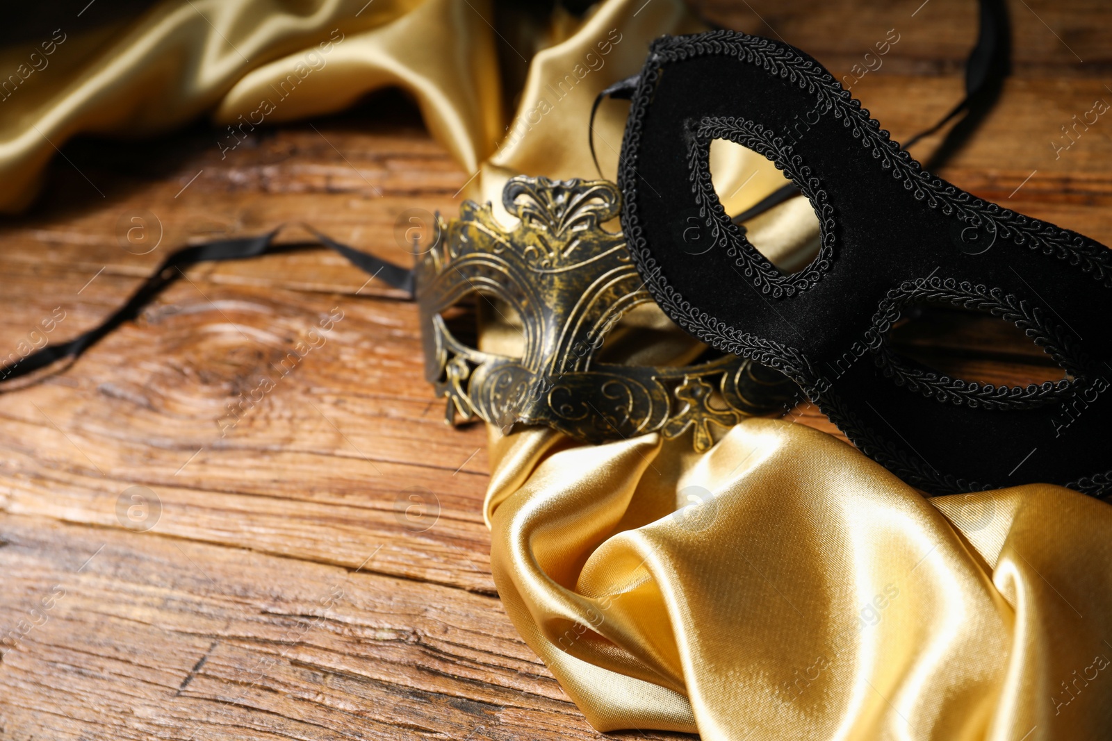 Photo of Beautiful carnival masks and silk fabric on wooden table, space for text