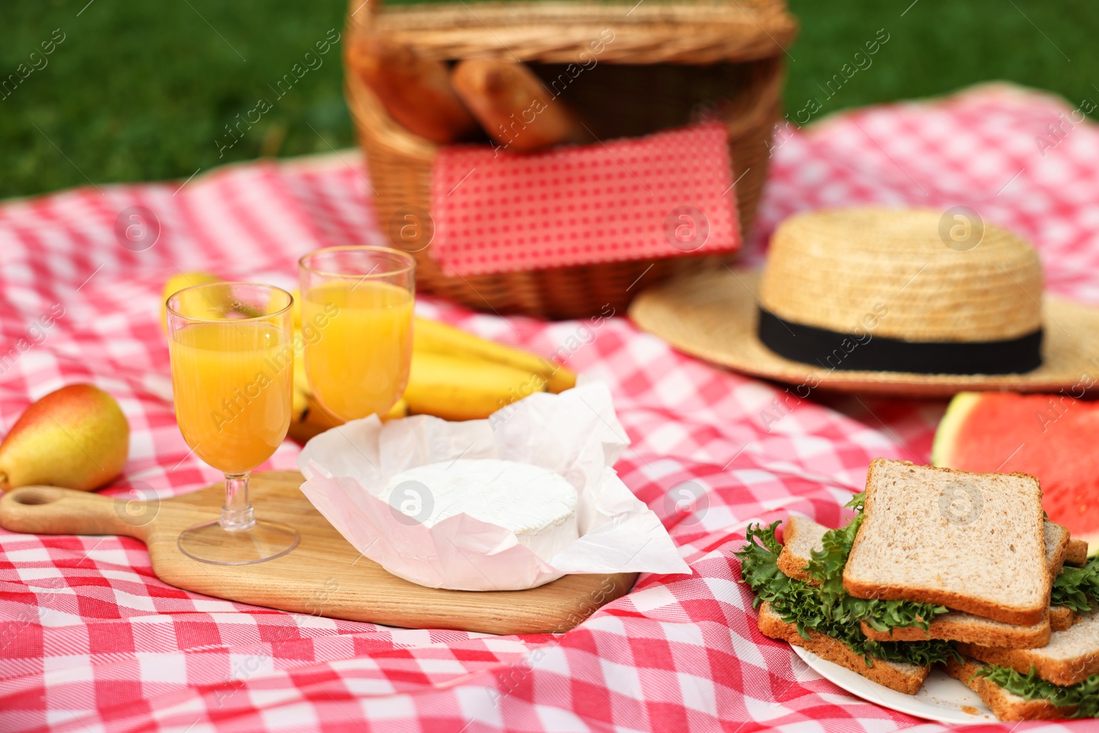 Photo of Different food, juice and hat on picnic blanket outdoors, closeup