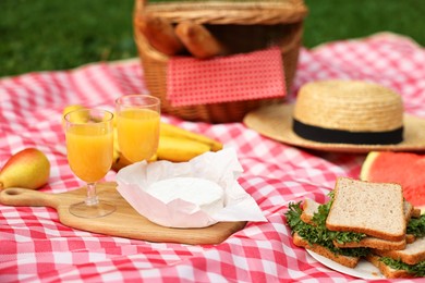 Different food, juice and hat on picnic blanket outdoors, closeup