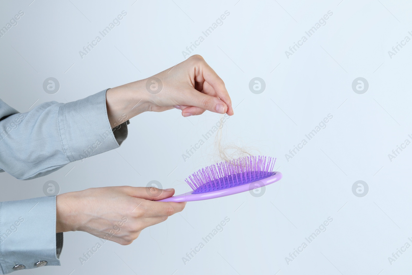 Photo of Woman taking lost hair from brush on light grey background, closeup. Space for text