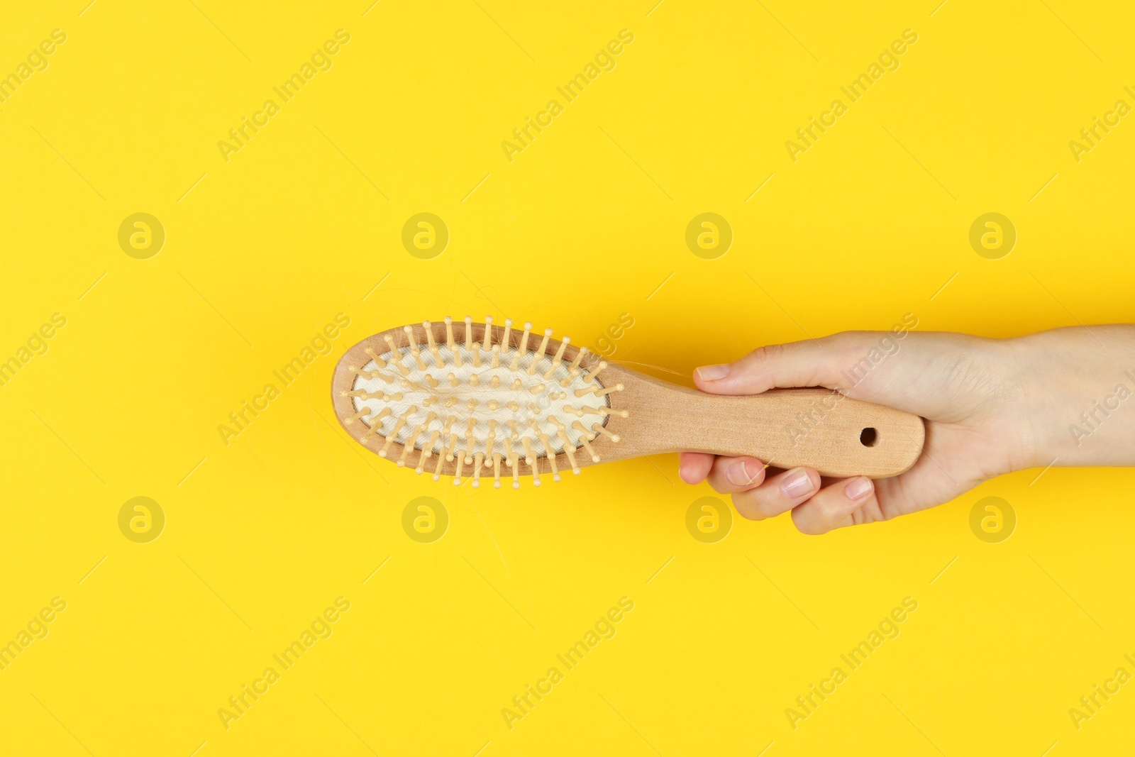 Photo of Woman holding brush with lost hair on yellow background, closeup