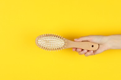 Woman holding brush with lost hair on yellow background, closeup