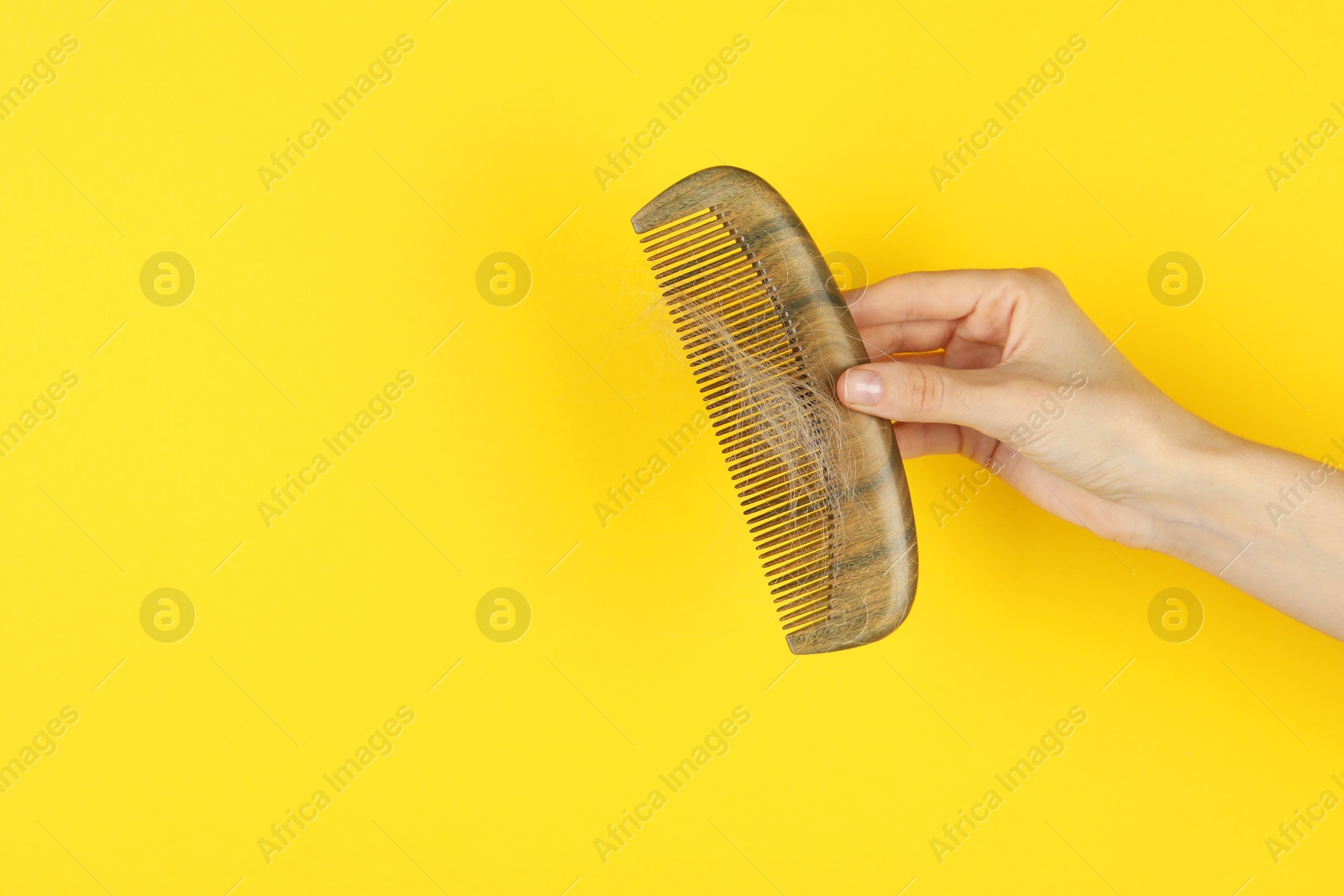 Photo of Woman holding comb with lost hair on yellow background, closeup. Space for text